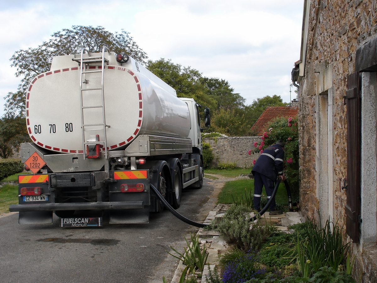 Un camion de livraison stationné devant une maison rurale. Le livreur prépare le tuyau pour remplir la cuve de fioul domestique d'un client qui a judicieusement anticipé ses achats suite à l'analyse des prévisions du prix du fioul sur le marché.
